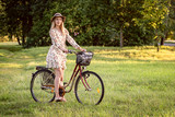 Young, slim, blonde woman on bicycle against defocused park landscape. Autumn color shade.