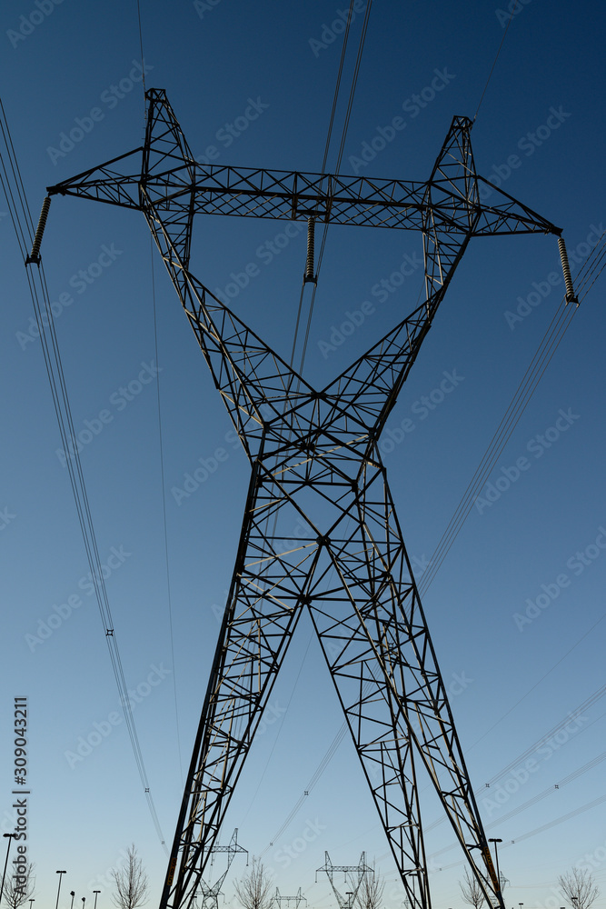 Silhouette of a steel lattice suspension electric tower with high tension power lines looks like a robot