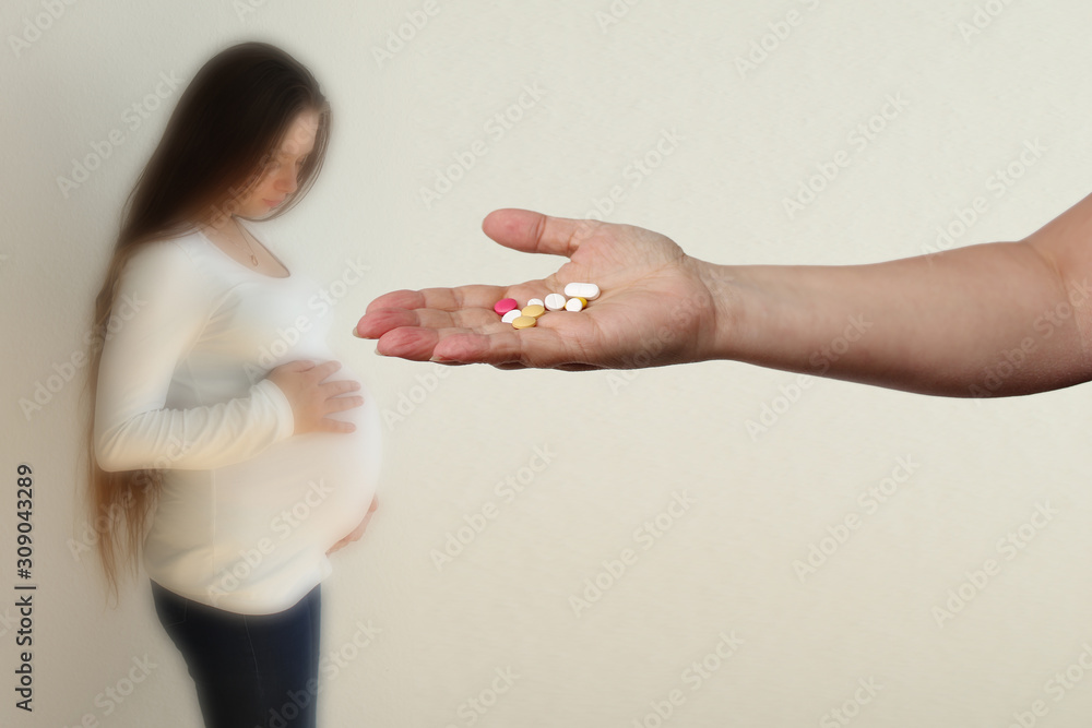 Naklejka premium female hand holds out, offering, a handful of colored pills and capsules, close-up, blurred image of a pregnant woman in the background, copy space, concept of pregnancy complications, treatment