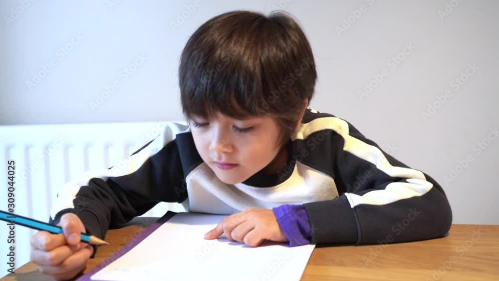 Portrait of adorable kid sitting alone doing homework with happy face, Cute child boy using pencil writing on white paper. Students doing spelling test at home.Homeschooling concept Portrait of adorable kid sitting alone doing homework with happy face, Cute child boy using pencil writing on white paper. Students doing spelling test at home.Homeschooling concept