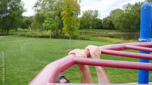 Man exercising, strength training, working out doing body weight underhand pull ups in the park in slow motion.