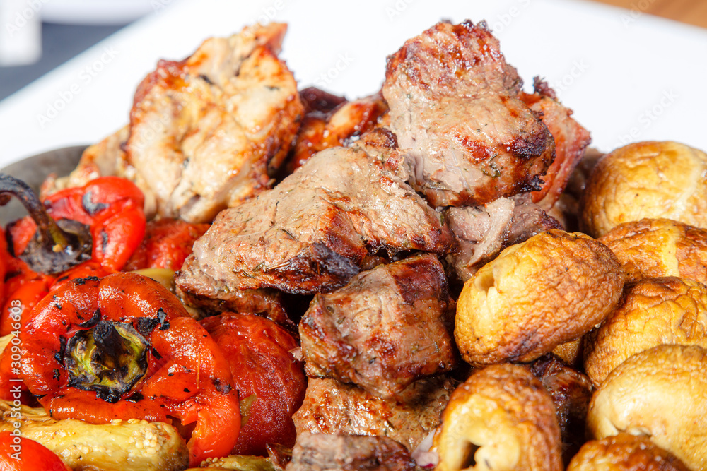 On a platter are meat, mushrooms and vegetables, fried on the grill. On a platter are meat, mushrooms and vegetables, fried on the grill.