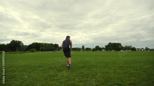 In shape man running on green field, throwing a football, practicing, training, working out and improving in slow motion.