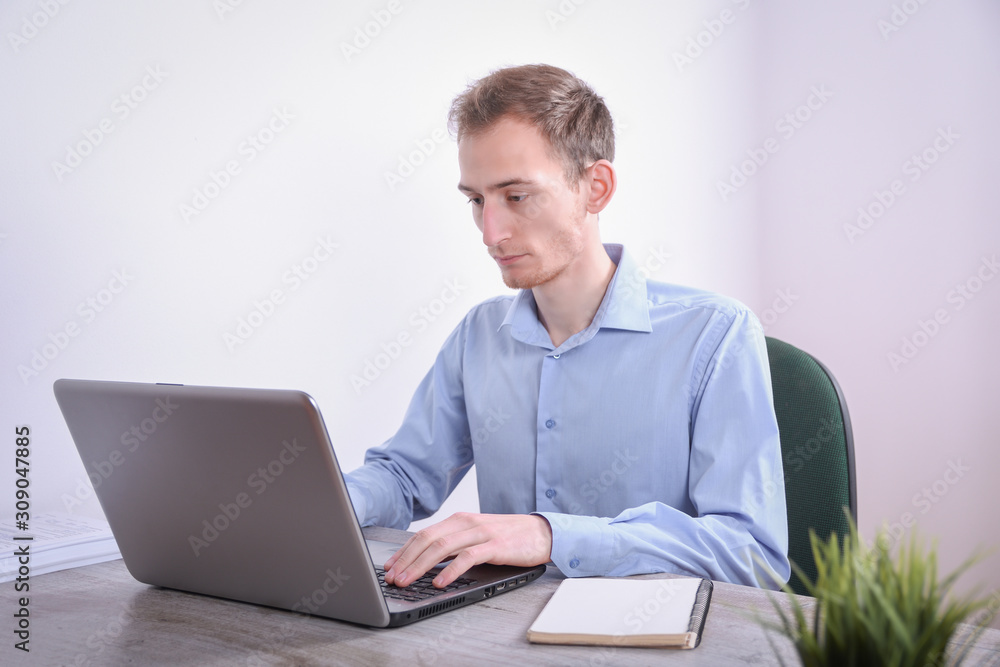 Portrait of young business man sitting at his desk desktop laptop technology in the office.Internet marketing, finance, business concept Portrait of young business man sitting at his desk desktop laptop technology in the office.Internet marketing, finance, business concept