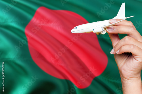 Bangladesh travel concept. Woman holding a miniature plane on national flag background. Holiday and voyage theme with copy space for text.