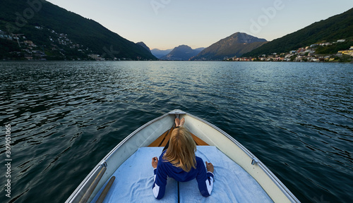 Una mujer tumbada en una barca disfrutando de las vistas al lago y montañas. photo