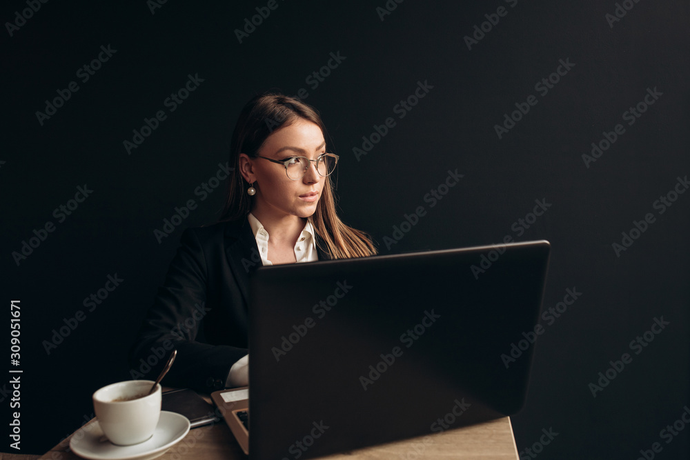 a beautiful girl wearing in office clothes with sunglasses sitting in the cafe with laptop and phone on the table a beautiful girl wearing in office clothes with sunglasses sitting in the cafe with laptop and phone on the table