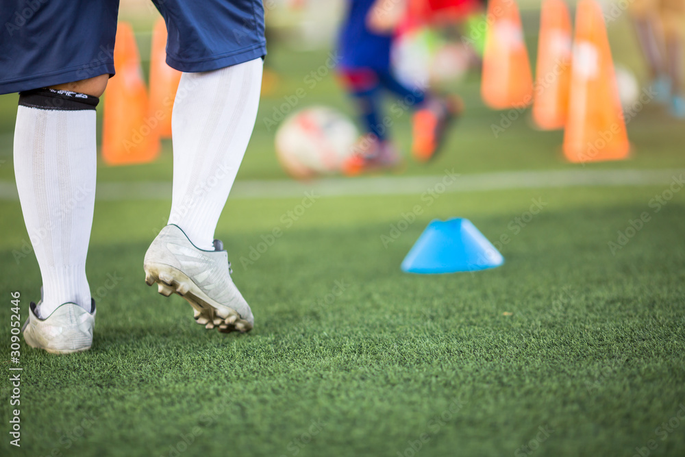 Obraz premium Young boy soccer player is standing with blurry marker cone on green artificial turf. It is activity on holiday. Football training in academy.