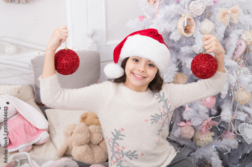 Playful mood. Cheerful kid. Creating festive atmosphere. Child decorating christmas tree with red ball. Girl kid decorating christmas tree. Kid in santa hat decorating christmas tree. Good vibes