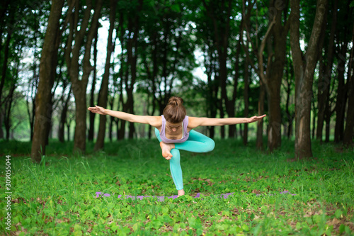 A young sports girl practices yoga in a quit green summer forest, yoga assans posture. Meditation and unity with nature