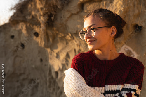 Sunny portrait of attractive young brunette girl in glasses and sweater enjoying summer sunny day outdoor