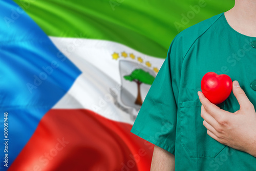 Equatorial Guinea veterinary clinic concept. Veterinarian is holding plastic heart in green uniform on national flag background. Animial love theme. photo