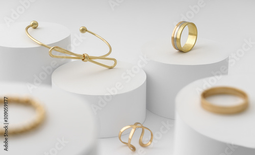 Modern Golden bow shape bracelet and rings collection on white cylinders platform photo