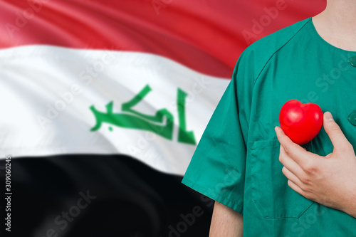 Iraq veterinary clinic concept. Veterinarian is holding plastic heart in green uniform on national flag background. Animial love theme. photo