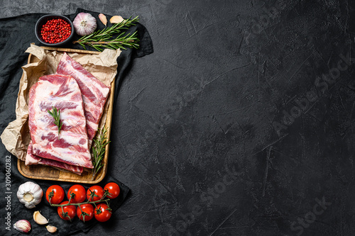 Fresh raw pork ribs with rosemary and garlic in a wooden bowl. Black background. Top view. Space for text