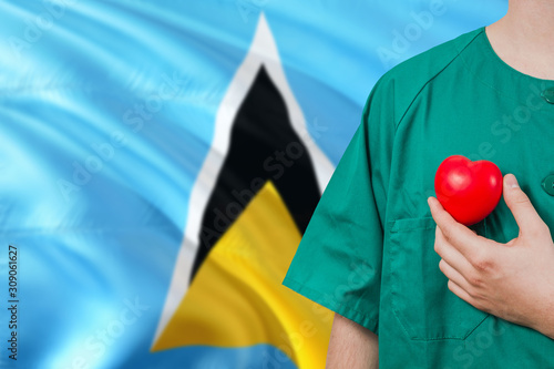 Saint Lucia veterinary clinic concept. Veterinarian is holding plastic heart in green uniform on national flag background. Animial love theme. photo