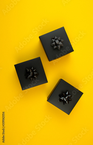 Black gift boxes with bow on yellow background.
