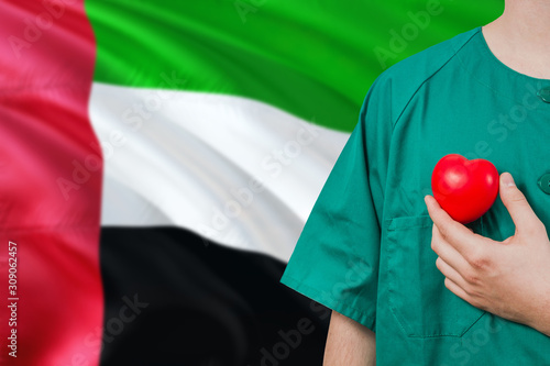 United Arab Emirates veterinary clinic concept. Veterinarian is holding plastic heart in green uniform on national flag background. Animial love theme.