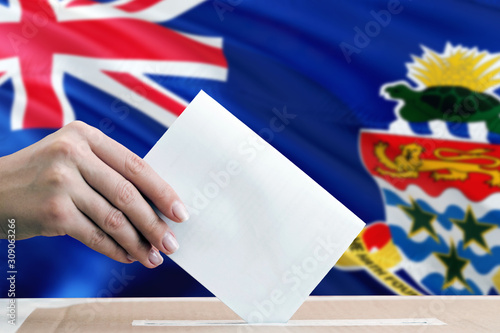 Cayman Islands election concept. Side view woman putting a ballot in a box on national flag background.