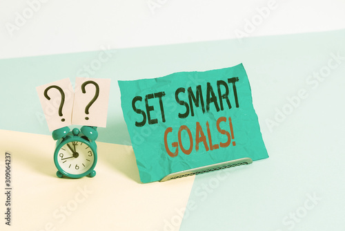 Conceptual hand writing showing Set Smart Goals. Concept meaning list to clarify your ideas focus efforts use time wisely Alarm clock beside a Paper sheet placed on pastel backdrop