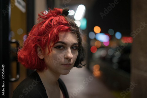portrait of a woman with half red hair looking into the camera with bokeh background
