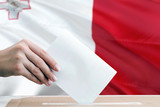 Malta election concept. Side view woman putting a ballot in a box on national flag background.