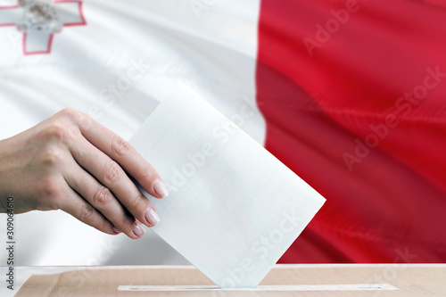 Malta election concept. Side view woman putting a ballot in a box on national flag background.