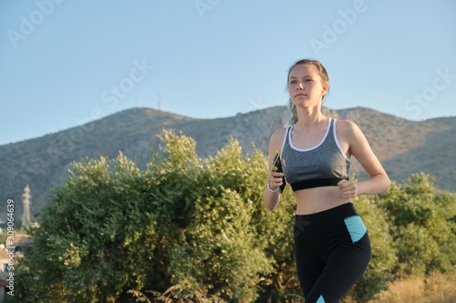 Running young teenager girl in fitness clothes headphones with smartphone