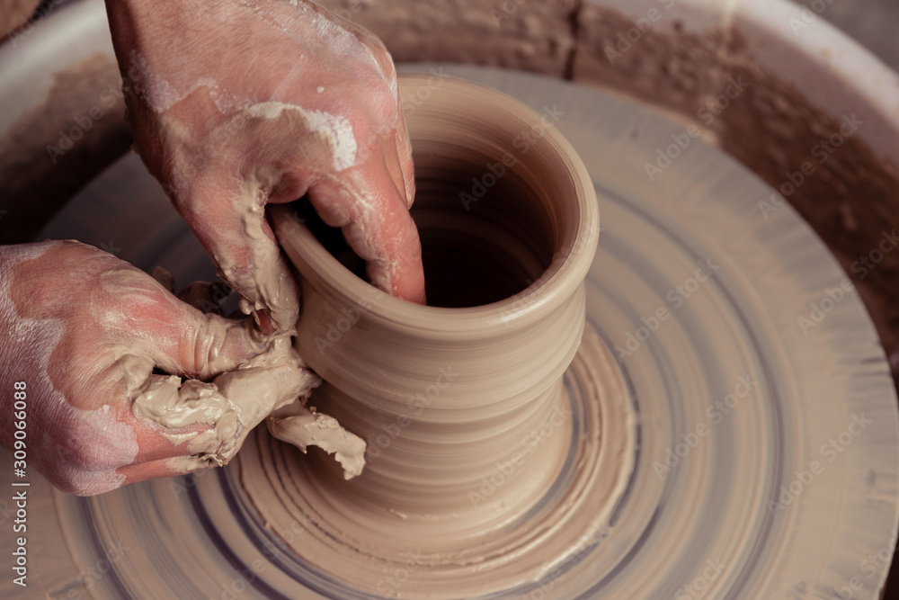 close-up dirty hands of potter man creating with fingers and pressure an earthen jar pot of white clay on the potter's wheel circle in studio