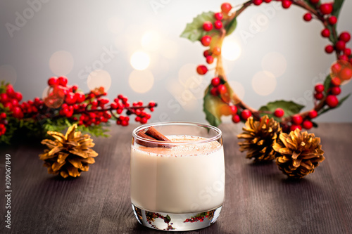 Traditional Christmas cocktail Eggnog with eggs, alcohol, grated nutmeg and cinnamon closeup. Sweet traditional drink on wooden table with red decorations and pine cones