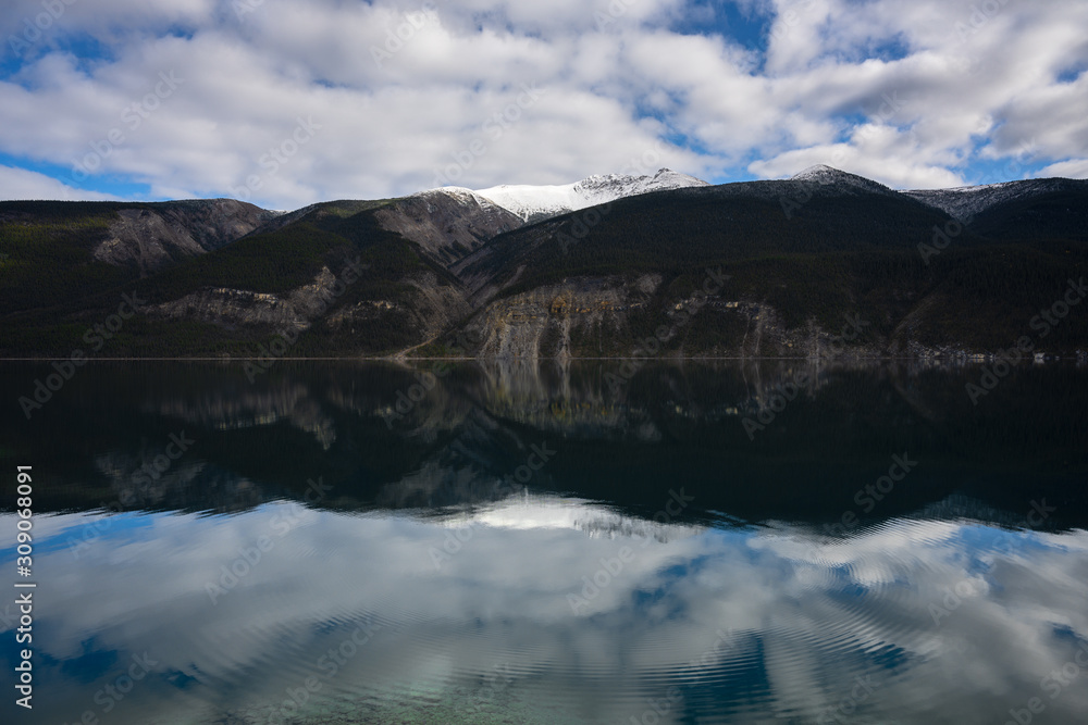 Breathtaking mirror photography with mountain peaks, forestry and cloudy sky reflecting in lake with circular waves