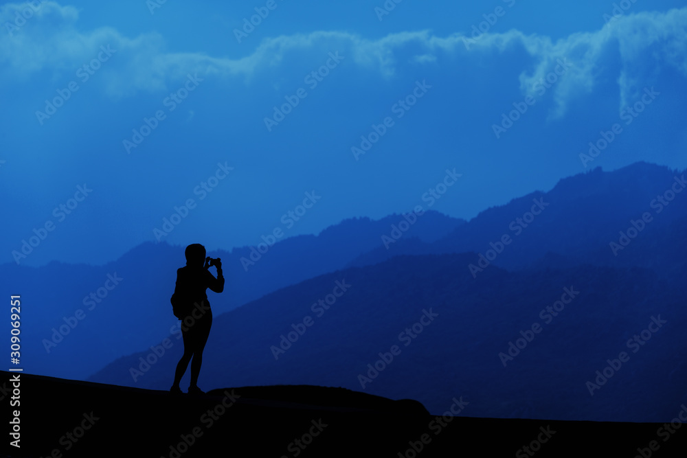 Young tourist woman standing on top of mountain and looking at a beautiful landscape. Adult girl tourist relax on hill in summer epic sky up view. High peak tour Classic blue 2020 year color concept