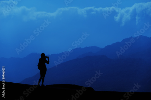 Young tourist woman standing on top of mountain and looking at a beautiful landscape. Adult girl tourist relax on hill in summer epic sky up view. High peak tour Classic blue 2020 year color concept