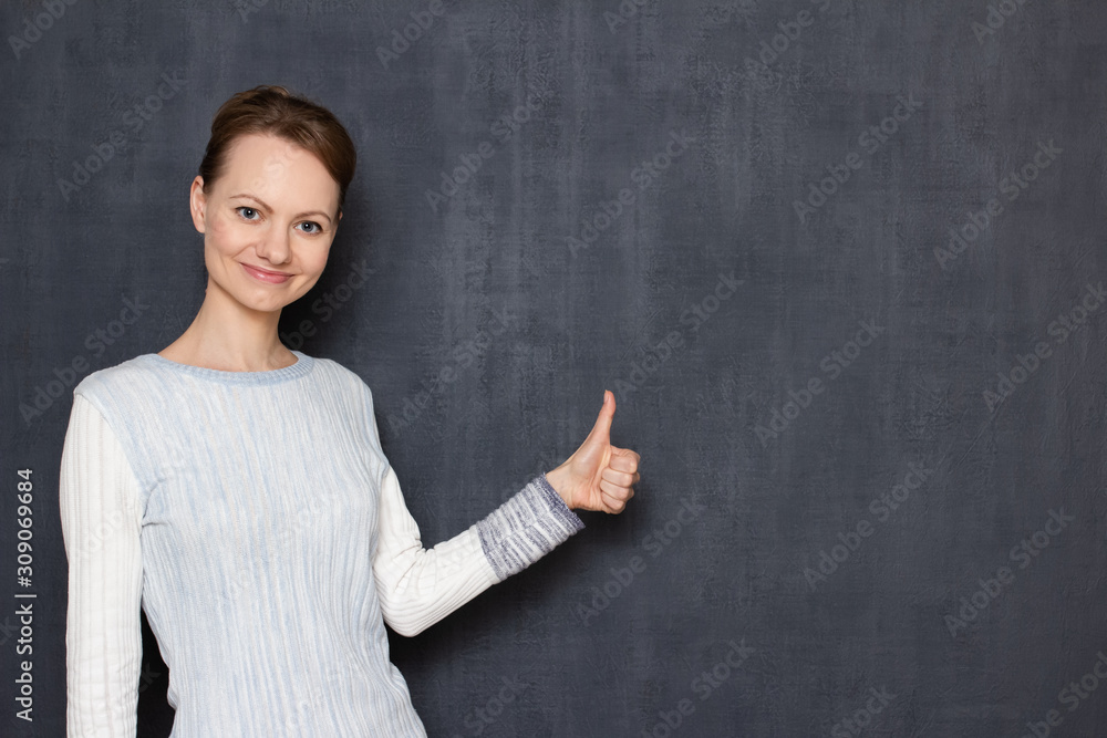 Portrait of happy pretty blond girl wearing jumper showing thumb up Portrait of happy pretty blond girl wearing jumper showing thumb up