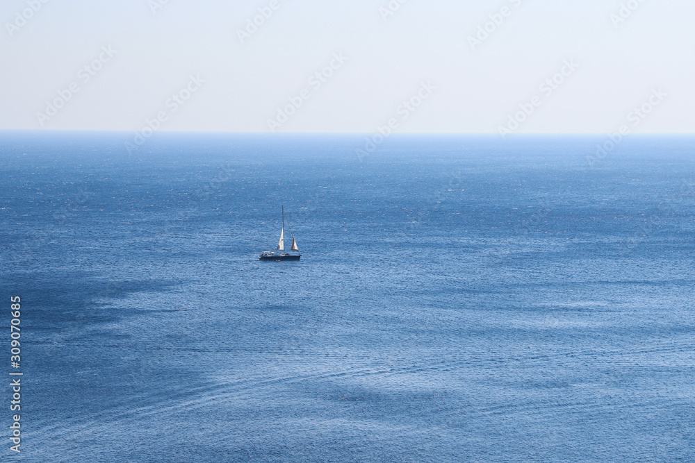 A small boat with a sail floats on the sea. A small boat with a sail floats on the sea.