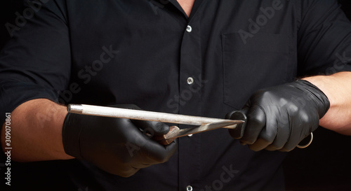 Foto chef in a black shirt and black latex gloves sharpen a kitchen knife on an iron