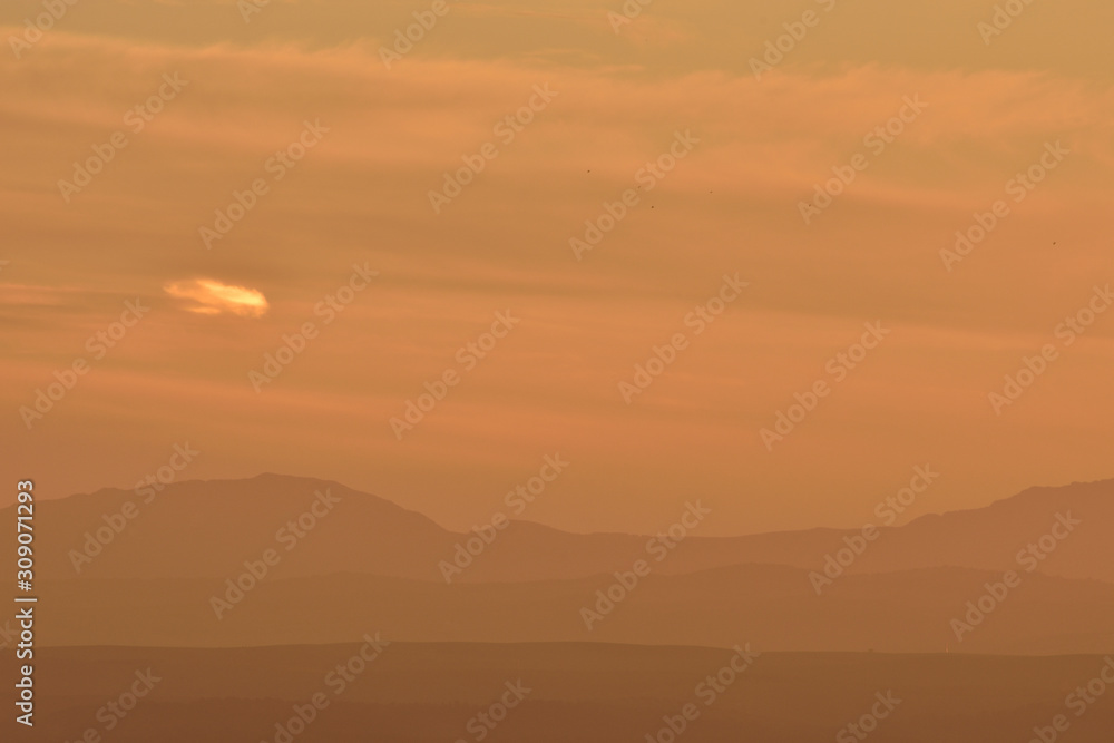 Silhouette of several hills on the horizon with orange sunset light and small lonely cloud in the sky