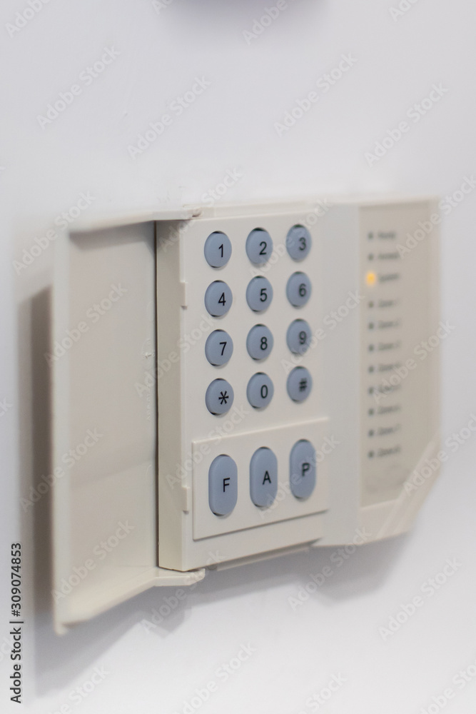 A regular security systems keypad with buttons and a plastic flap mounted on a white wall A regular security systems keypad with buttons and a plastic flap mounted on a white wall