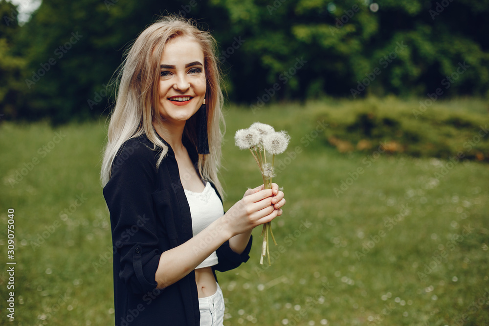 Pretty girl standing in a park. Lady in a white t-shirt and black shirt. Woman with blonde hair. Girl with flowers; Pretty girl standing in a park. Lady in a white t-shirt and black shirt. Woman with blonde hair. Girl with flowers;
