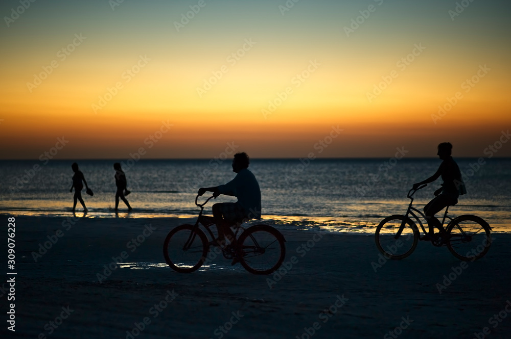 Riding bike on Holbox island beach in sunset Mexico. People cycling on the Caribbean beach at sunset.