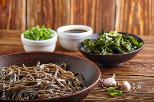 Still life of traditional japanese soba noodles with nori (edible seaweed) and soy sauce, on a wooden surface closeup with selective focus