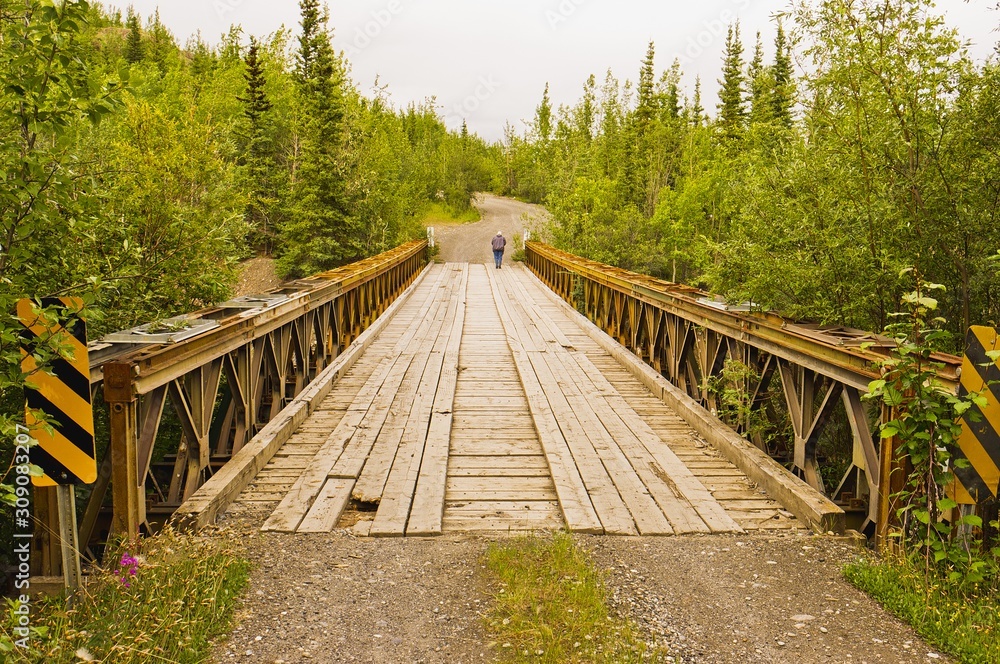 Fototapeta premium Person walking along an old steel construction bridge in Yukon, Canada