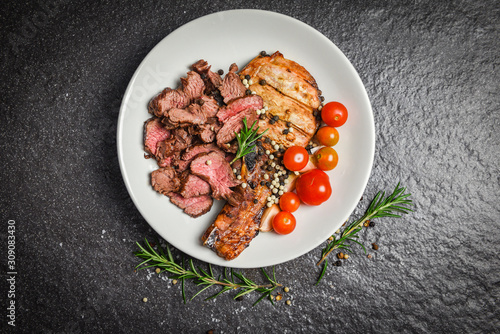 Fototapeta Naklejka Na Ścianę i Meble -  Roasted beef steak fillet and pork chops with herb and spices serve with vegetable on white plate - grilled beef meat slice on black background