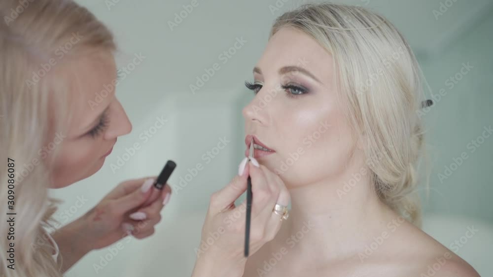 Medium shot makeup artist carefully appling soft pink lipstick to womens lips with brush of lipstick Medium shot makeup artist carefully appling soft pink lipstick to womens lips with brush of lipstick