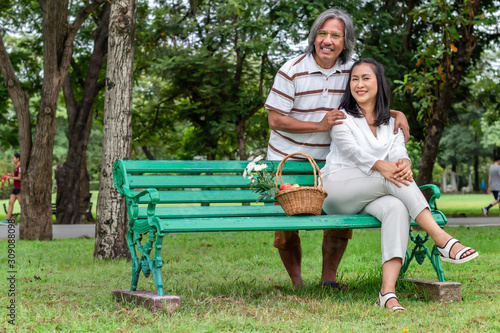 Happy elderly Asian Couple with fruit basket in park.