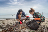 Problems of environmental pollution and oceans, a young couple in orange gloves cleans plastic and garbage in a black trash bag on a tropical beach in Thailand.