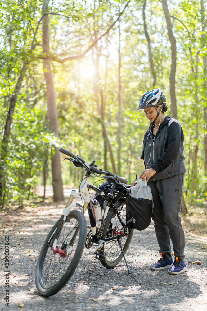 Senior asian woman riding bikes in park with hold map on trip