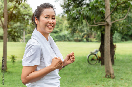 Middle Asian aged woman smiling and jogging in the park.
