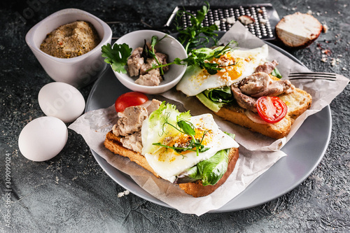 Close-up sea food sandwich. Cod liver, fresh lettuce, pea sprouts, tomatoes and fried eggs. Healty and tasty breakfast on a cutting wooden board.