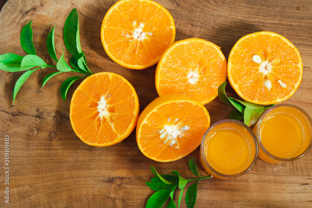A piece of mandarin orange fruit sliced with leaves on the golden teak floor And two orange juice glasses. As a background image. A piece of mandarin orange fruit sliced with leaves on the golden teak floor And two orange juice glasses. As a background image.
